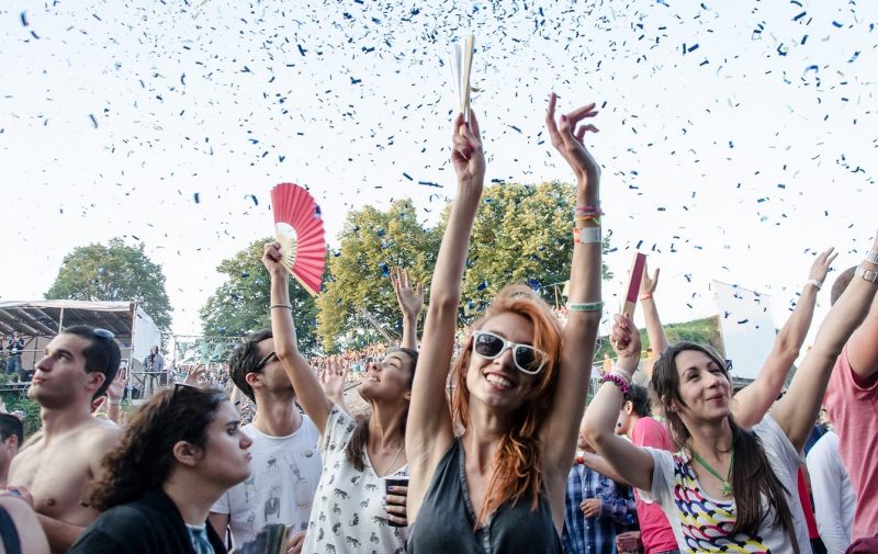 Crowd of people dancing at a festival with their arms up, while confetti rains down