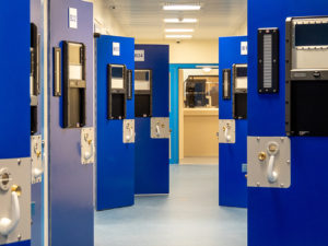 A view through the Eastern PIC custody block past open cell doors with the custody desk in the background.