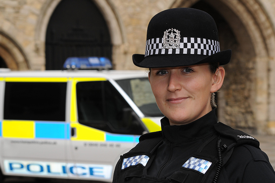 A police officer is stood in the foreground in uniform, with a police van and the Southampton Bargate behind her.