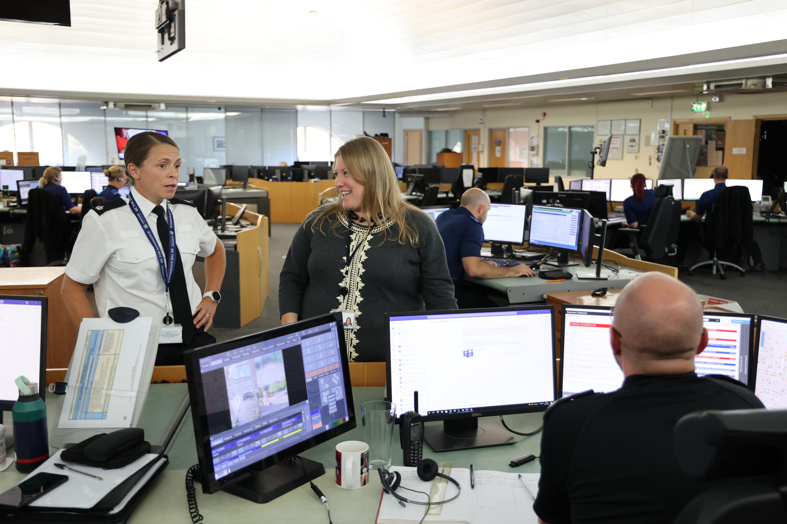 Donna Jones smiling speaking to a police officer in a call centre behind some computer screens of those taking calls.