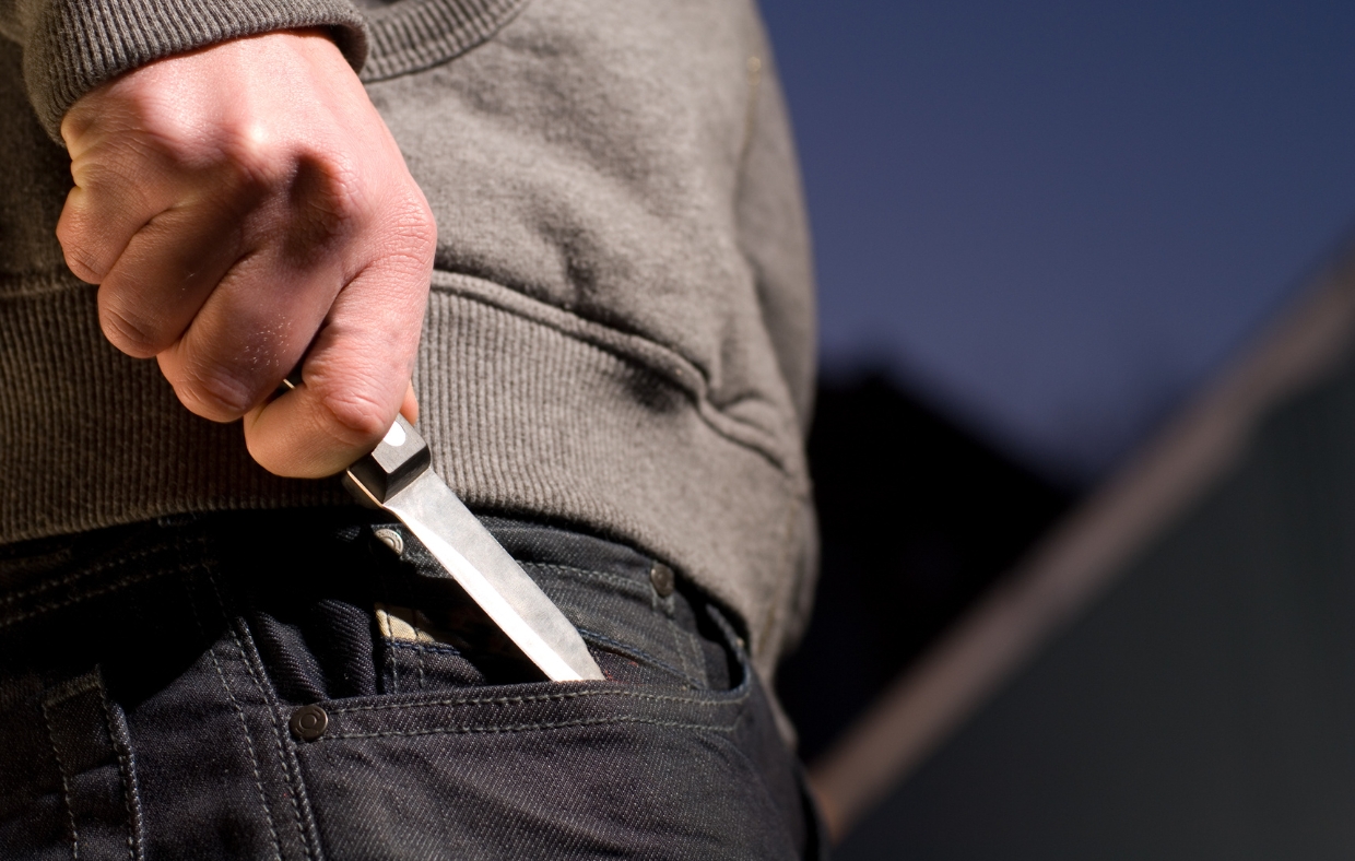 A man pulling a small knife from his pocket. Close up on his hand.