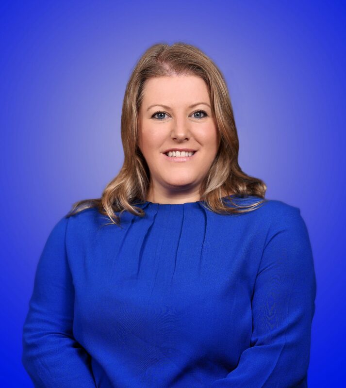 Donna Jones smiling in a blue dress in front of a blue background