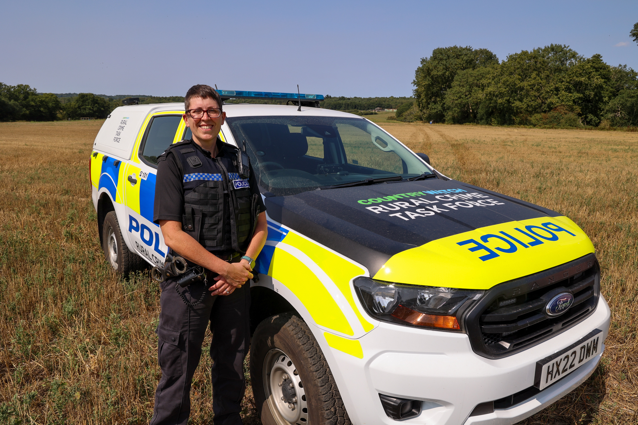 A uniformed police officer stood next to a 4x4 police vehicle in a field on a sunny day.