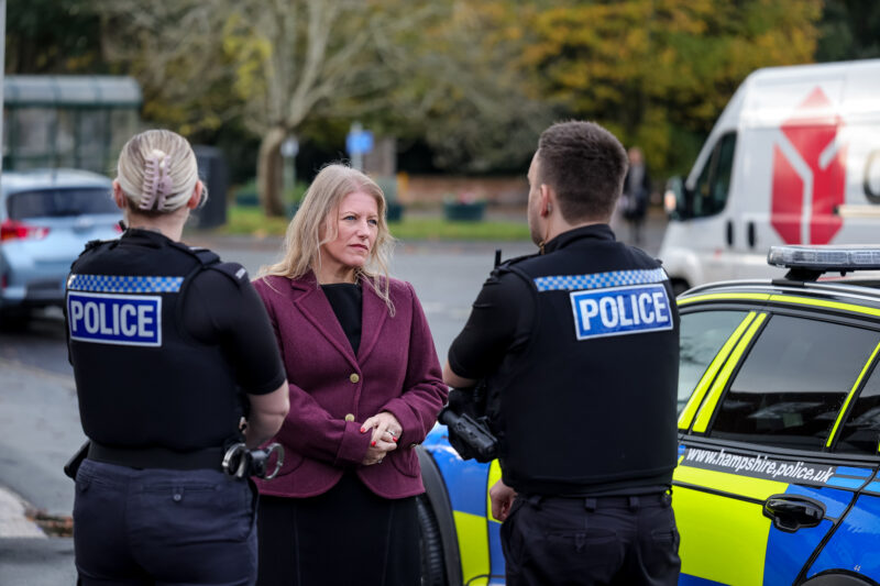 Donna Jones in a purple Jacket talking to two police officers next to a police car