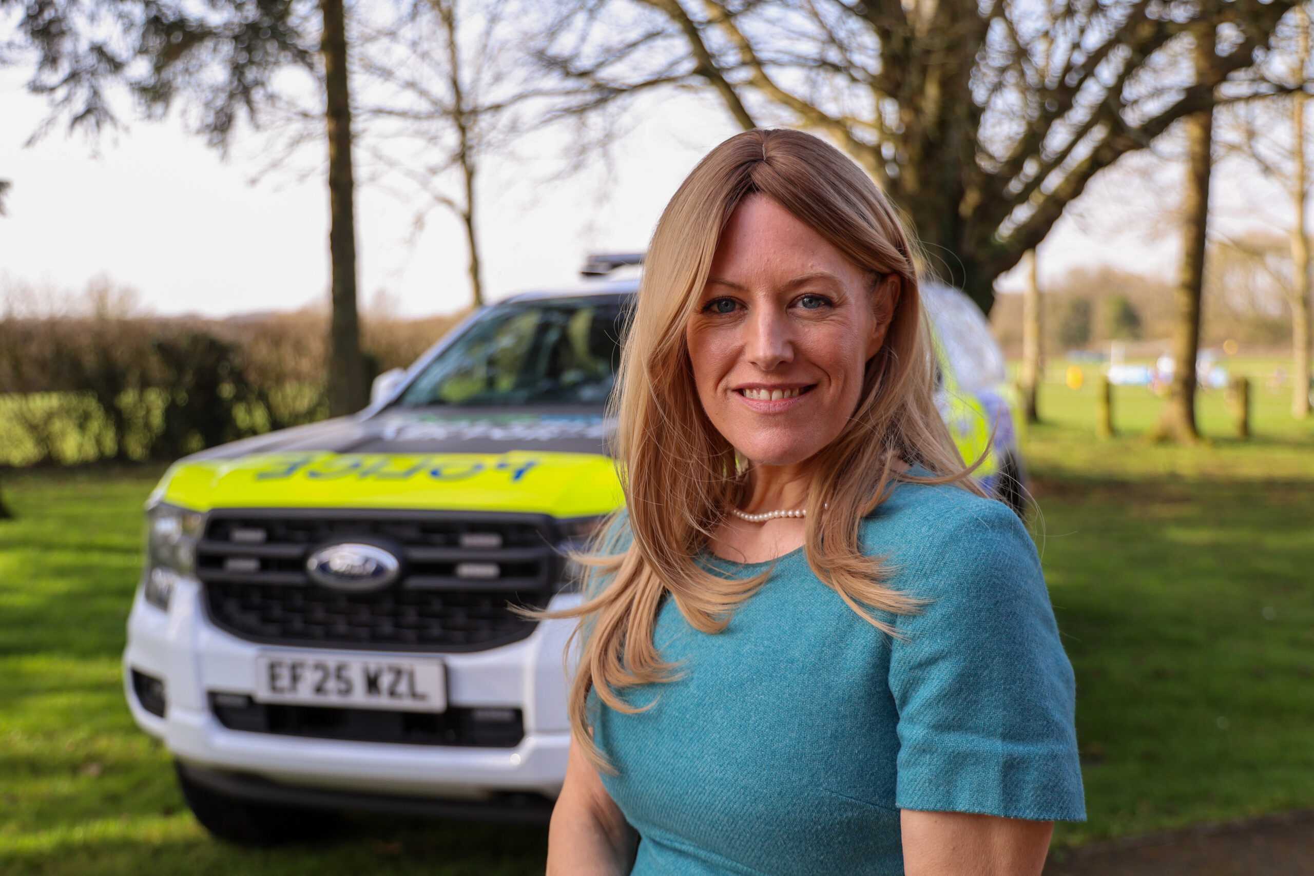 PCC Donna Jones smiling at the camera and standing in front of a police vehicle in a rural setting