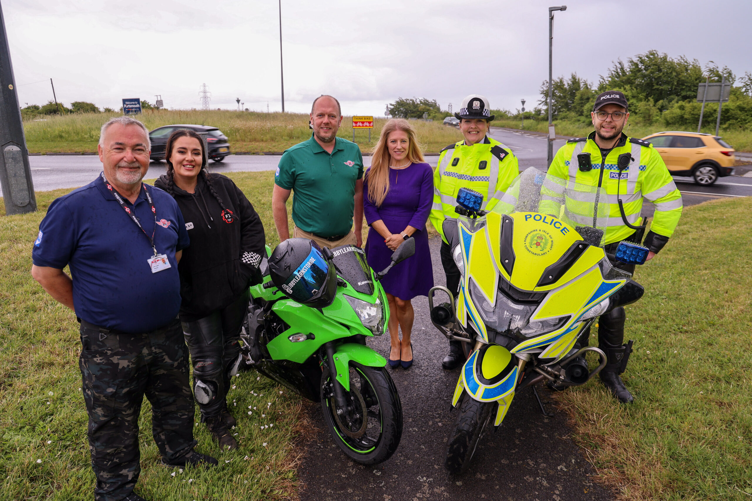 PCC Donna Jones stood next to a busy roundabout, alongside three volunteers from DocBike and two uniformed police officers. There is a police motorbike in front of them all.