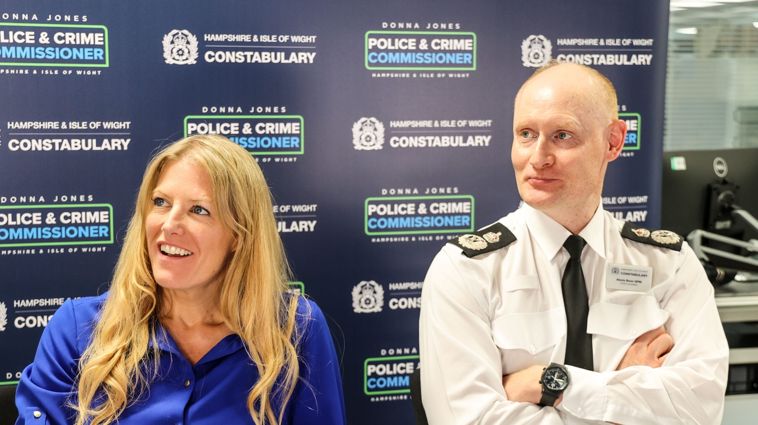 PCC Donna Jones and Chief Constable Alexis Boon, both smiling, sat in front of a board with repeated OPCC and Constabulary logos on it.
