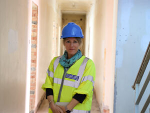 PCC Donna Jones in a yellow high-visibility jacket and a blue hard hat, stood in the corridor of a derelict building.