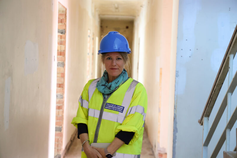 PCC Donna Jones in a yellow high-visibility jacket and a blue hard hat, stood in the corridor of a derelict building.