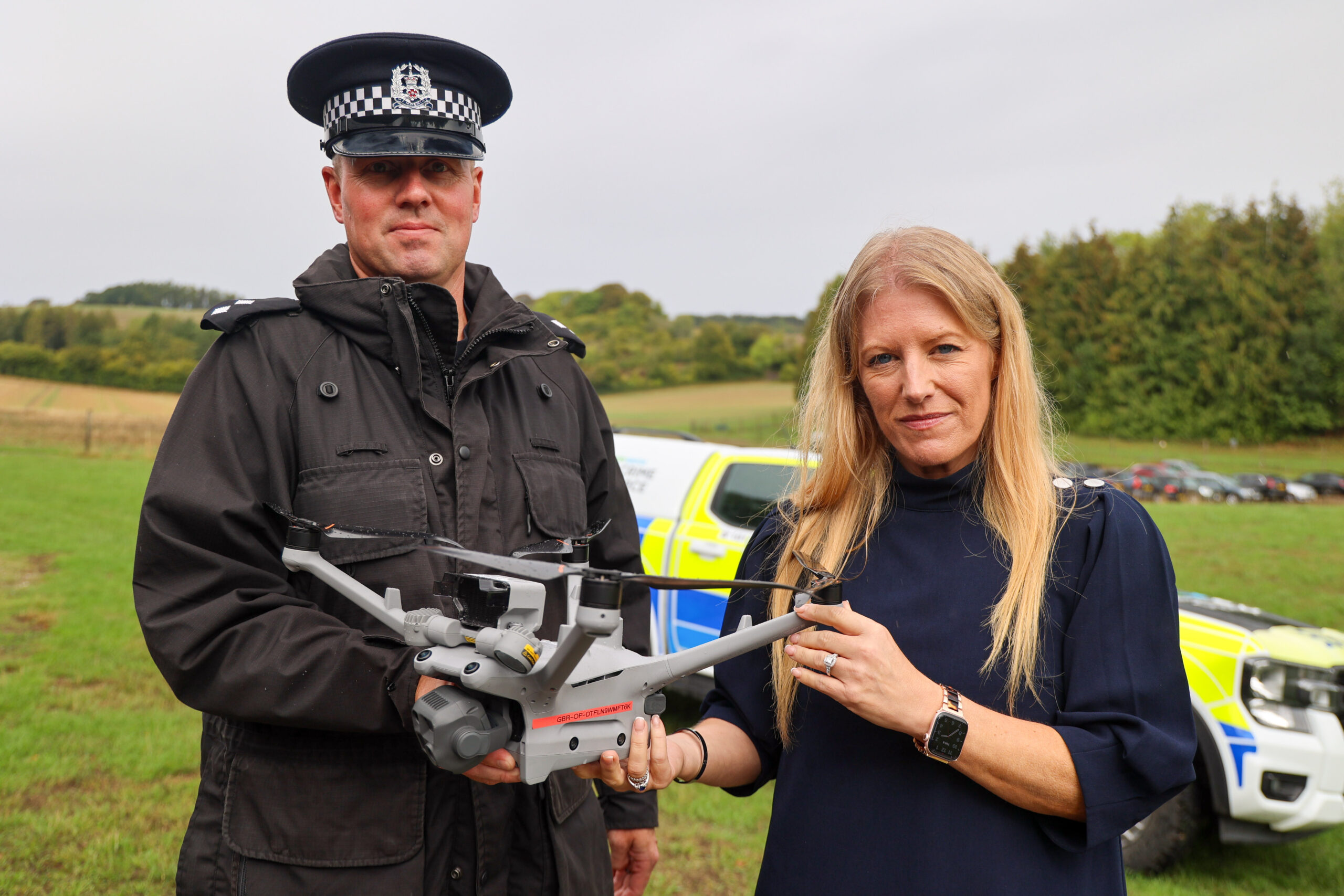 Insp Stuart Ross & PCC Donna Jones in a field holding a police drone with a police car behind them